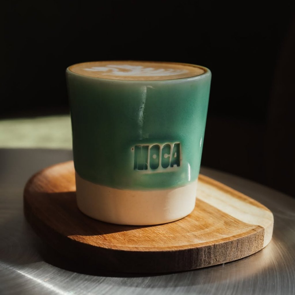 Cafe con leche en taza de ceramica verde de Moca sobre tabla de madera, con luz de manana